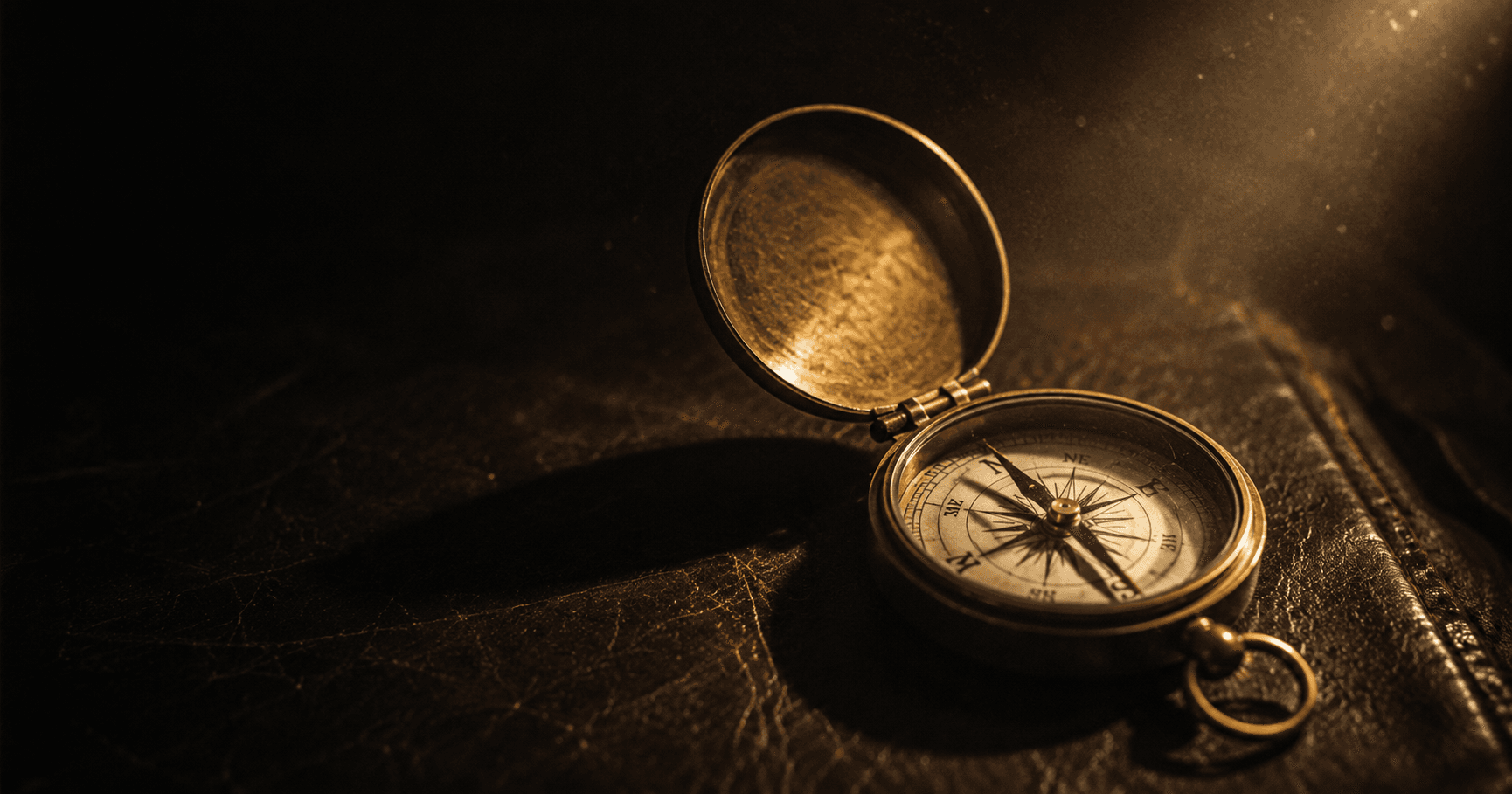 An antique brass compass lying open on dark leather, lit by a single warm-gold beam — a first bearing taken before a journey begins.